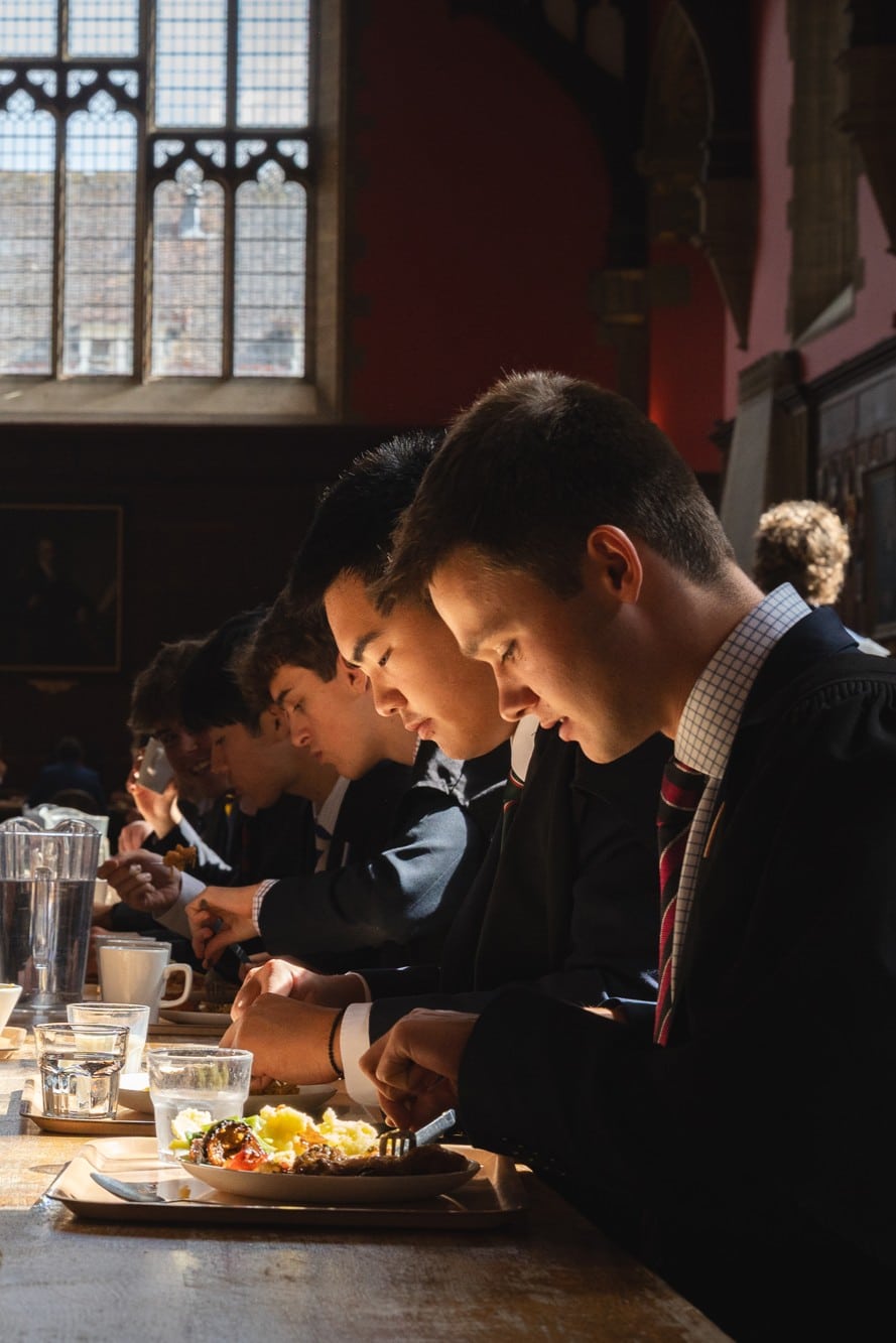 Boy eating in a grand dining Hall at Radley College whilst smiling